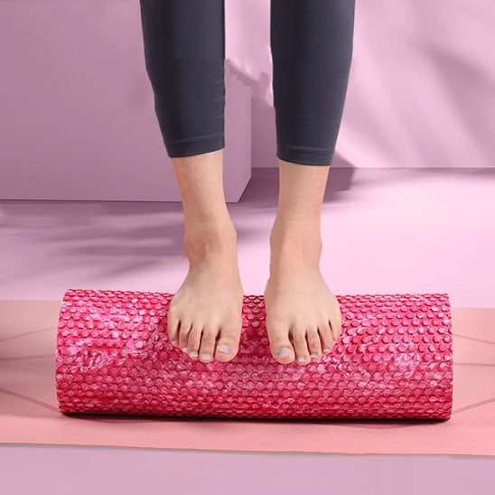 Deux pieds posés sur un rouleau de massage, sur tapis rose.