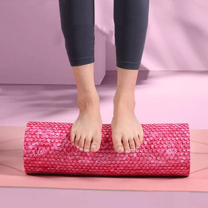 Deux pieds posés sur un rouleau de massage, sur tapis rose.