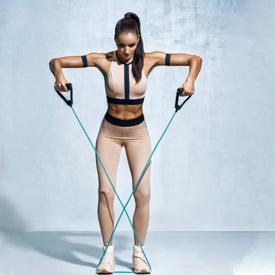Femme croisant un élastique musculation au sol, bras tendus latéralement.