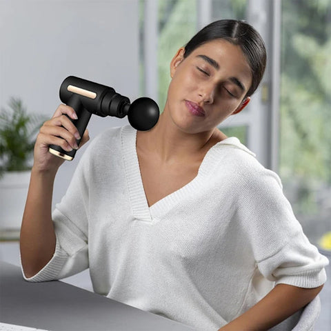femme utilise un pistalet de massage sur son épaule droite
