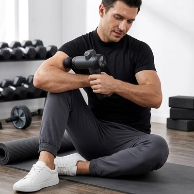 Homme assis utilisant un pistolet de massage sur son biceps.