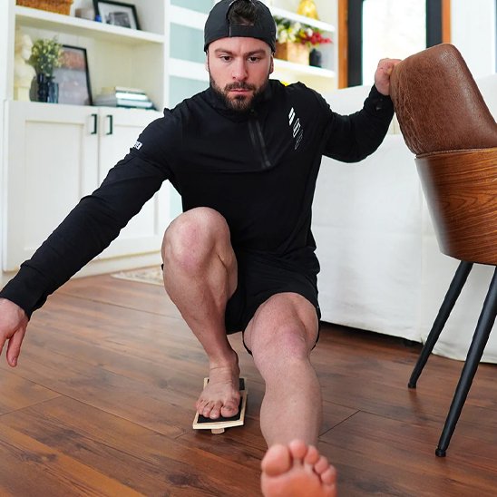 Homme s'entraînant sur planche d'équilibre tenant une chaise.