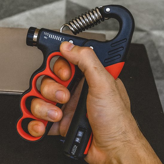 Main serrant un hand grip sur table en arrière plan.