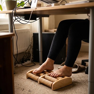 Pieds nus sur un rouleau de massage en bois, sous le bureau.