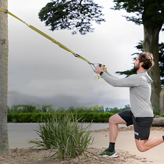 Un homme s’entraîne dehors avec Sangle musculation fixée sur arbre.