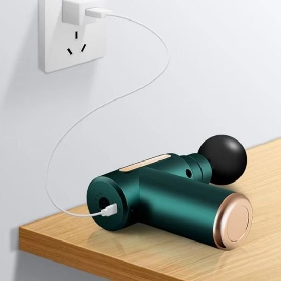 un Pistolet de massage vert posé sur étagère en charge via câble USB mural.