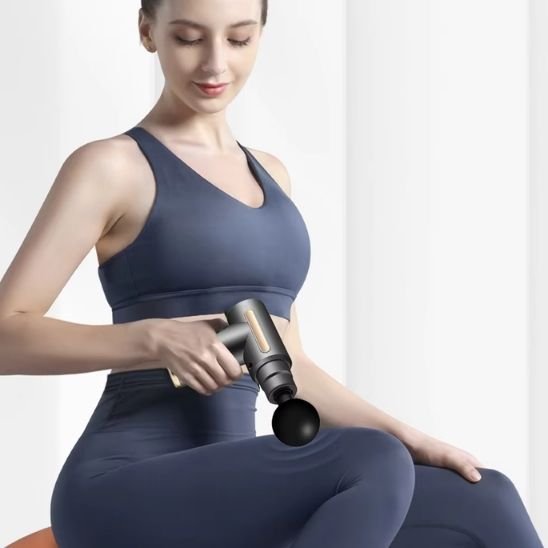 une femme assise utilise un pistolet de massage gris  sur la cuisse