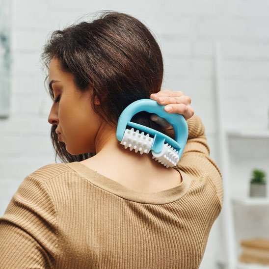 Une femme masse sa nuque avec un rouleau a domicile.